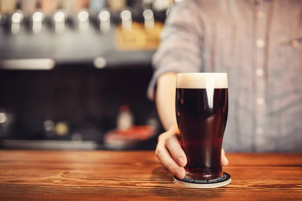 Barman houdt glas donker bier klant achter houten bar teller — Stockfoto