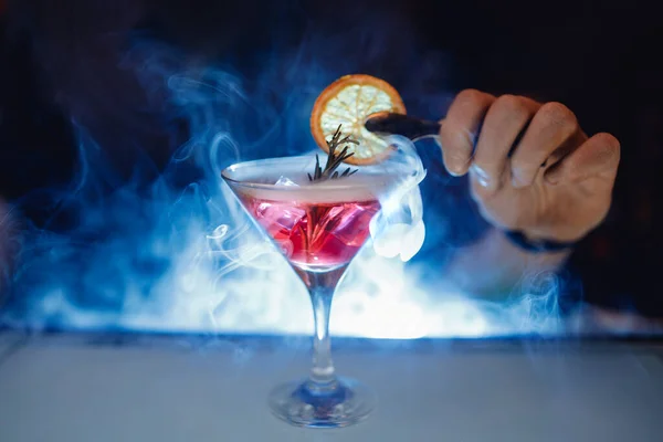 Бармен сделать красный алкогольный коктейль с дымом в стекле, украшенный оранжевым — стоковое фото