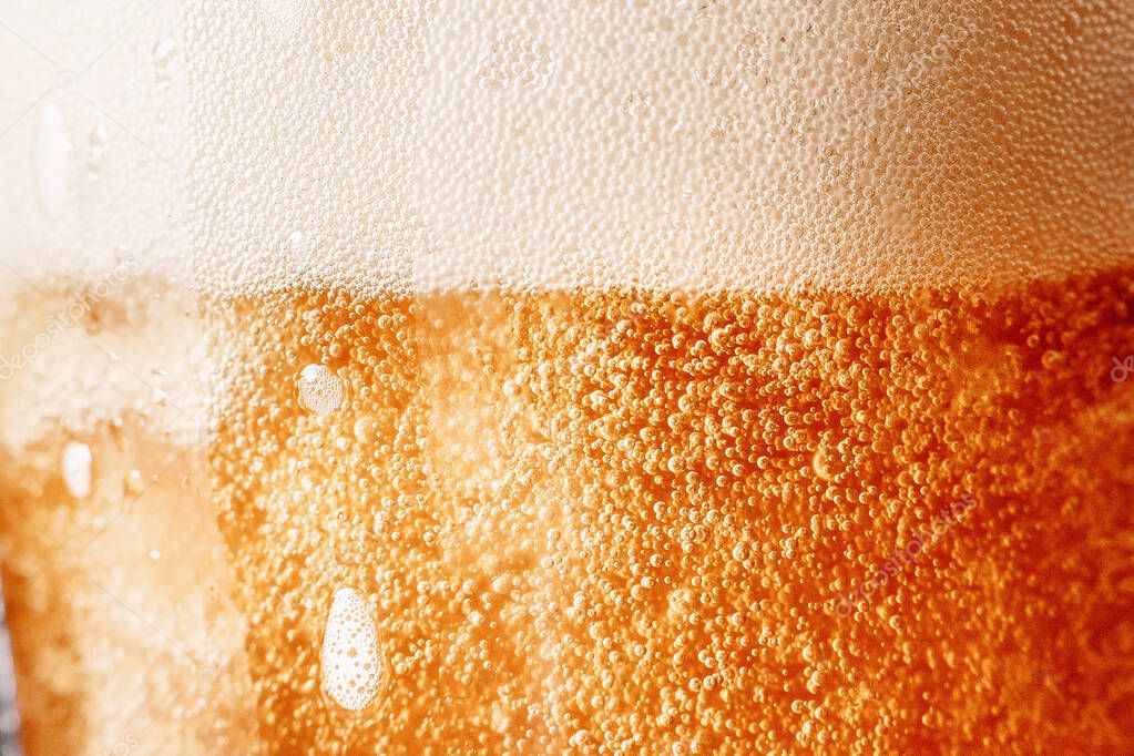 Close up gold background texture of yellow lager beer with froth and bubbles in glass, soft focus