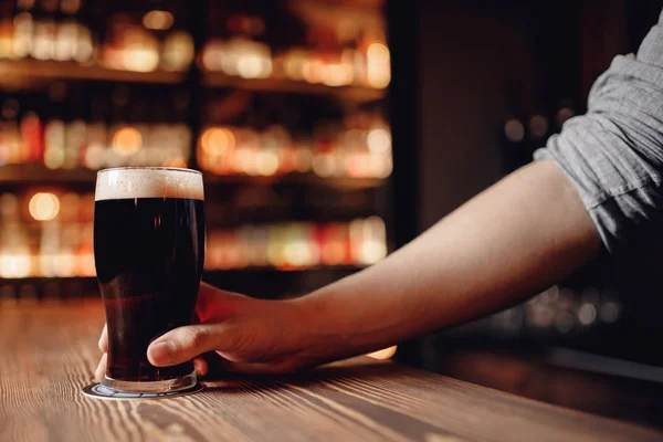 Barman houdt glas donker bier klant achter houten bar teller — Stockfoto