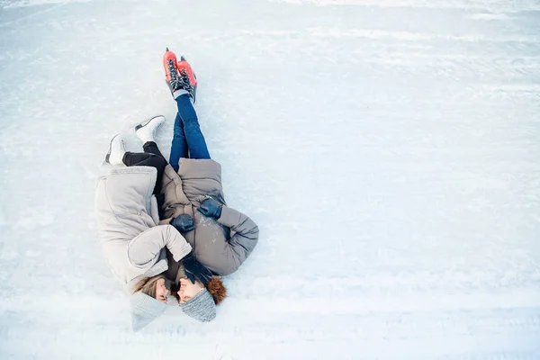 Chica y chico acurrucarse en la nieve en patines pista de hielo en invierno, vista superior. Pareja amante vacaciones — Foto de Stock