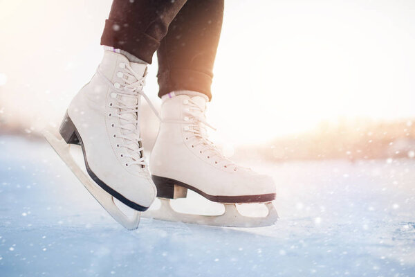 Winter active holiday concept. Girl is standing on ice in white figure skates, snow flakes, sunlight
