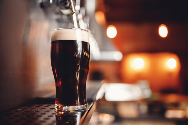 Dark Draft cold beer pour in glass from crane in pub