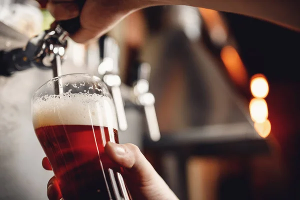 Barman schenkt ambachtelijke drank bier uit kraan in glas, donkere achtergrond — Stockfoto