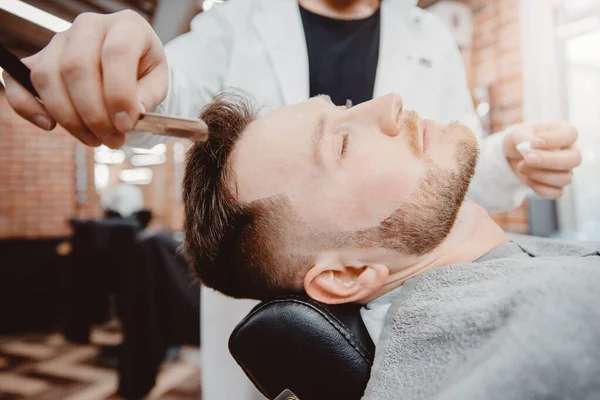 Il parrucchiere barbiere tiene il rasoio per la barba, il cliente maschile è seduto sulla sedia — Foto Stock