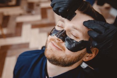 Erkekler için kaplıca ve cilt bakımı. Berber profesyonel müşteriye siyah kömür maskesi takıyor.