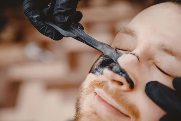 Spa y cuidado de la piel para hombres. Peluquero profesional aplica máscara de carbón negro al hombre cliente — Foto de Stock