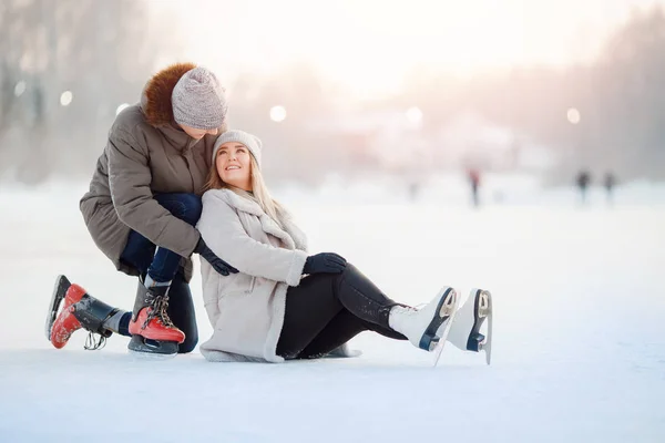 L'uomo aiuta la ragazza ad alzarsi dalla neve sulla pista di pattinaggio, caduta infortunio invernale. Concetto prima conoscenza, pagamento dell'assicurazione — Foto Stock