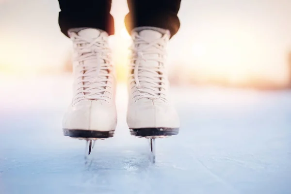 Conceito de férias ativas de inverno. Mulher em pé no gelo em patins figura branca, flocos de neve por do sol — Fotografia de Stock