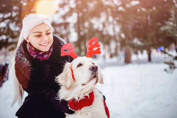 Happy young woman hugs dog golden retriever in winter day. Friendship concept