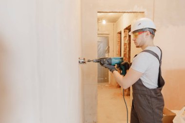 Pnömatik çekiç delici ve elmas kaplama delgisi olan tamirci elektrik kablosu, soket, anahtar için duvarda delik açıyor.