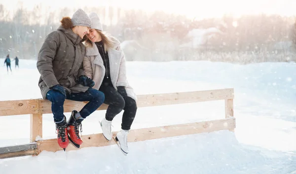 Actividades al aire libre de invierno. Amor pareja chica y joven hombre pista de patinaje sobre hielo, en el fondo la luz del sol — Foto de Stock