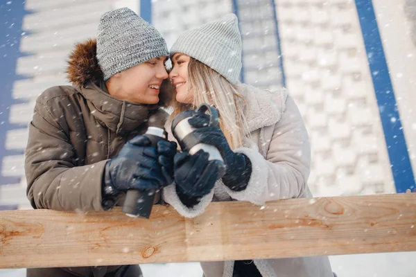 Casal amoroso bebe chá quente ou café de canecas térmicas na rua de inverno na pista de gelo — Fotografia de Stock