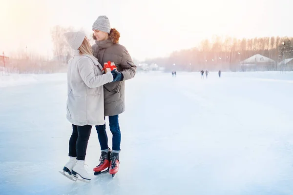 Uomo dando regalo scatola fidanzata inverno sulla pista di pattinaggio, sorpresa romantica per San Valentino o Natale. sfondo neve tramonto — Foto Stock
