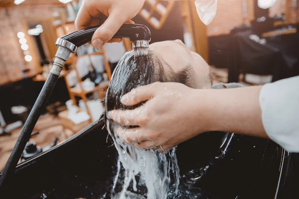 Парикмахер стирает волосы клиенту в парикмахерской — стоковое фото