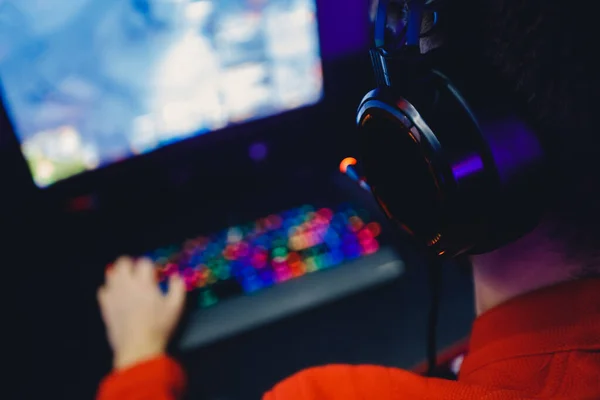 Jugador profesional jugando torneos de juegos en línea ordenador PC con auriculares, fondo rojo y azul borrosa — Foto de Stock