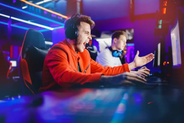 Streamer joven se regocija en la victoria jugador profesional jugando juegos en línea ordenador con auriculares, color neón —  Fotos de Stock