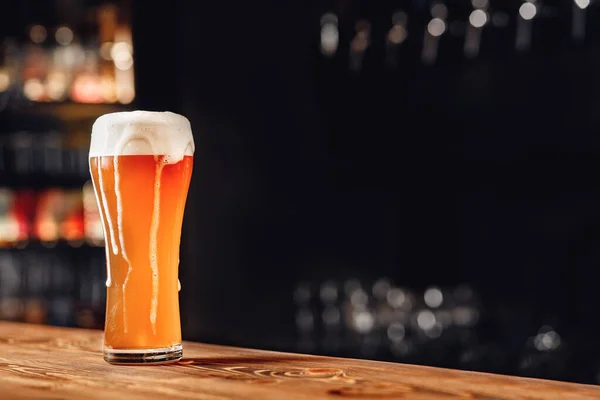 Fris licht bier met schuim houten kroeg teller, donkere achtergrond — Stockfoto