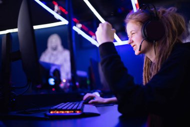 Flamalı güzel kız zafere seviniyor profesyonel oyuncu online oyun oynuyor kulaklıkla bilgisayar, neon rengi