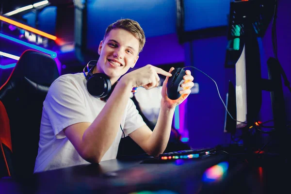 オンラインビデオゲームサイバースポーツマンのプロの若い男のプレーヤーは、コンピュータのためのヘッドフォン、キーボードとマウスを広告し、背景をぼやけている — ストック写真