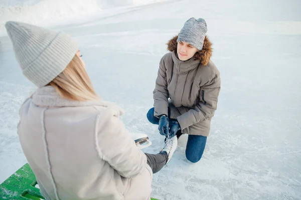 Homem ajuda a colocar em patins figura branca para a pista para bela jovem no fundo da neve no inverno, conceito é o amor de cuidado, relacionamento entre as pessoas — Fotografia de Stock