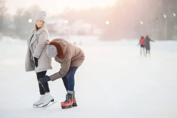 El hombre ayuda y sacude a la chica de la nieve después de caer en la pista de hielo en invierno. Concepto de cuidado y amor de pareja — Foto de Stock