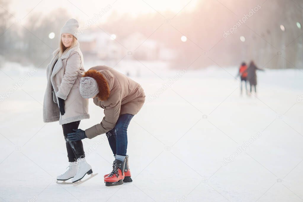 Man helps and shakes girl from snow after falling at ice rink in winter. Concept care and love of couple