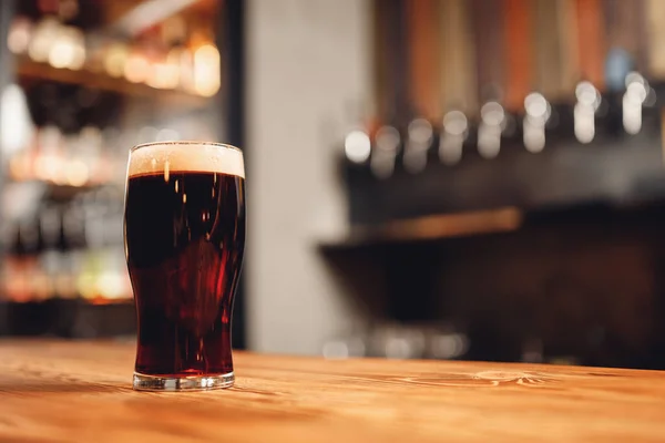 Glass with cold unfiltered dark beer on background of bar — Stockfoto