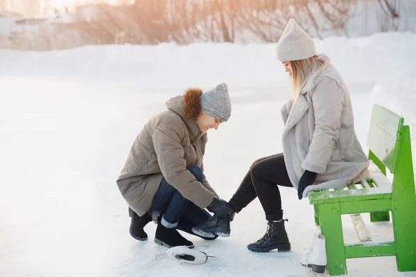 El hombre ayuda a ponerse patines de figura blanca para la pista de patinaje a la hermosa niña en el fondo de la nieve en invierno, el concepto es el cuidado del amor, la relación entre las personas — Foto de Stock