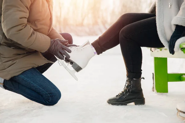 El hombre ayuda a ponerse patines de figura blanca para la pista de patinaje a la hermosa niña en el fondo de la nieve en invierno, el concepto es el cuidado del amor, la relación entre las personas — Foto de Stock