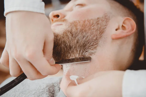 Kapper kapper houdt scheermes voor baard, mannelijke klant zit in stoel — Stockfoto
