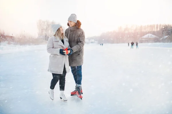 Sorpresa romantica per San Valentino o Natale. Uomo dando regalo scatola fidanzata inverno su pista di pattinaggio, sfondo neve tramonto — Foto Stock