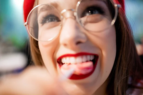 Cárie conceito e dano é perigo para o esmalte dentário. Rapariga comendo pau pegajoso doce na França café em boina vermelha e óculos — Fotografia de Stock