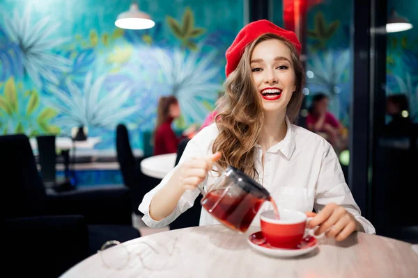 Junge hübsche Französin mit roter Baskenmütze wartet im Café auf die Bestellung von Kaffee und Croissant. Retro-Modekonzept — Stockfoto