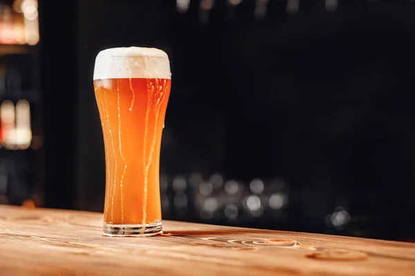 Lang glas fris licht bier met schuim op houten balie, donkere achtergrond — Stockfoto
