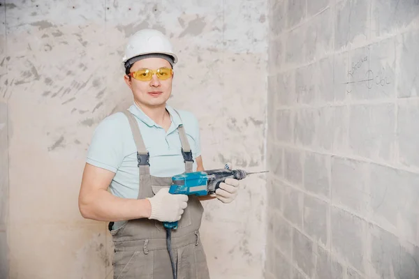 Portrait man builder repairer in protective glasses, hard hat, overalls showing having equipment in arm on grey background home brick — Stock Photo, Image