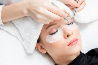 Kirpik uzatma prosedürü. Cımbız ustası güzel bir kadına sahte kirpik takar.