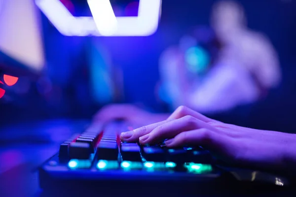 Profesional jugador en línea dedos de la mano teclado mecánico en neón color borroso fondo. Enfoque suave, vista trasera — Foto de Stock