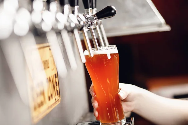 Jet van vers licht bier wordt gegoten in glazen beker op donkere achtergrond met spatten en schuim — Stockfoto