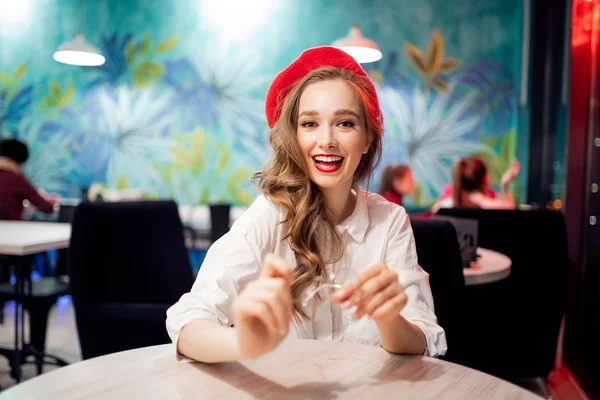 Porträt junge schöne Retro-Französin in roter Baskenmütze und weißem Hemd, Brille in der Hand, Frühstück im Café — Stockfoto