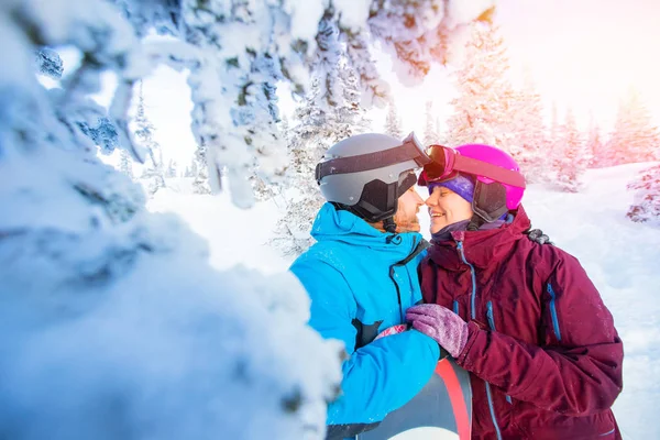 Pareja cariñosa en trajes abrazo y beso en el fondo del bosque de invierno. Concepto de vacaciones de esquí familiar — Foto de Stock