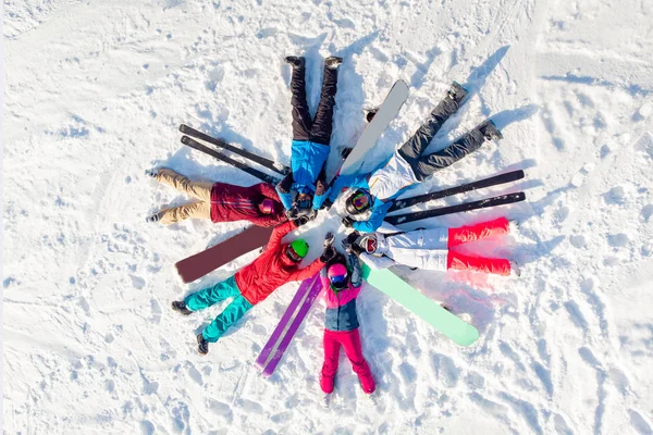 Feliz equipo de amigos esquiadores y snowboarders que se divierten y yacen círculo en la nieve con tablas de snowboard y esquí. Vista superior aérea —  Fotos de Stock