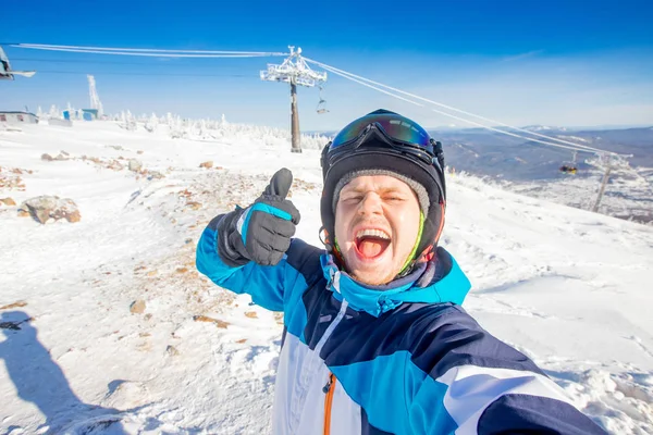 若い男性スキーヤーの笑顔は、保護ヘルメット、晴れた日、青空の冬のスキー場を背景に自撮り写真を作る — ストック写真