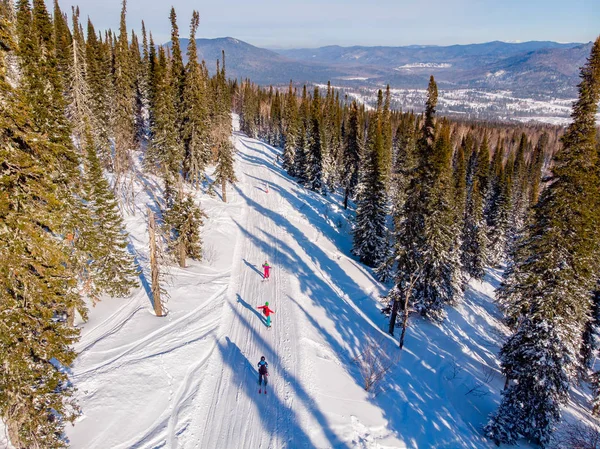 Grupa przyjaciół snowboardziści i narciarze jeździ po torze przez las, widok z lotu ptaka — Zdjęcie stockowe
