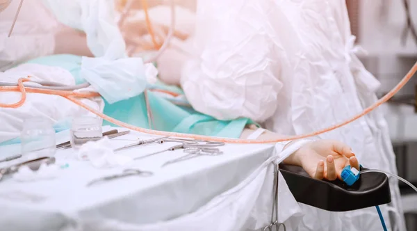 Mano del paciente en la mesa de operaciones, los médicos son personas operadas. Fondo azul claro —  Fotos de Stock