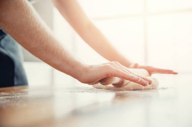 Şef, mutfak arka planında pizza hamuru yuvarlıyor.