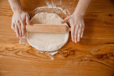 Şef ellerinin ahşap arka planda hamuru yuvarlamasının en üst görüntüsü