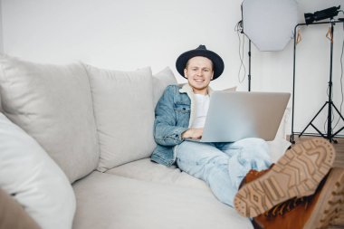 Şapka video blogunda serbest çalışan fotoğrafçı dizüstü bilgisayarda çalışır, seyahat hakkında video yükler, arka plan ışıklandırma ekipmanları