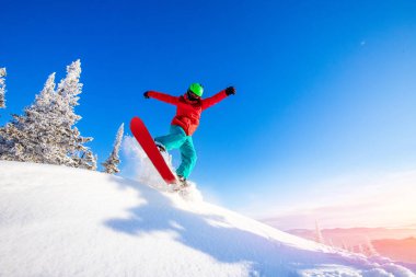 Tepeden aşağıya masmavi bir gökyüzüyle uçan snowboardcu.