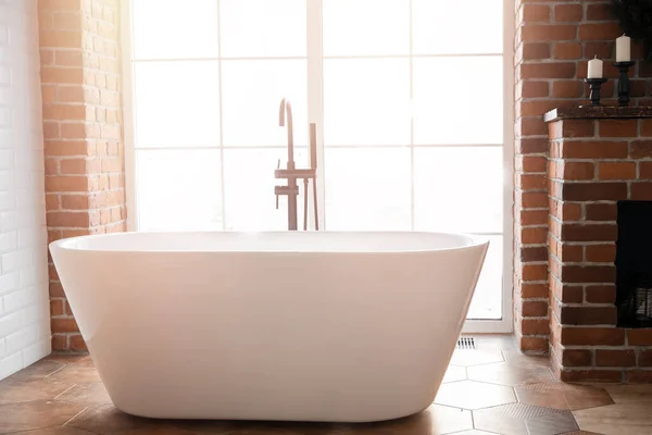 Modernes Badezimmer mit freistehender weißer Acryl-Badewanne und schwarzer Loft-Armatur. Wände aus Ziegeln, Parkett auf dem Boden, Sonnenlicht aus dem Fenster — Stockfoto